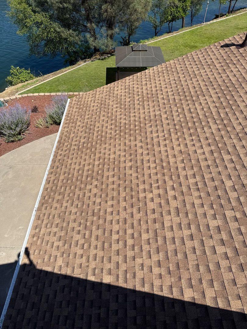 Completed roof with clean shingle lines, landscaping and lake below