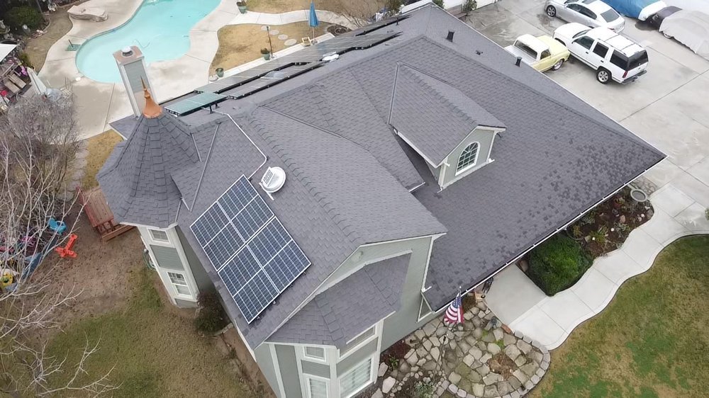 Aerial view of a completed Econo Roofing residential project featuring dark architectural shingles with rooftop solar panel array, pool and landscaped yard visible.